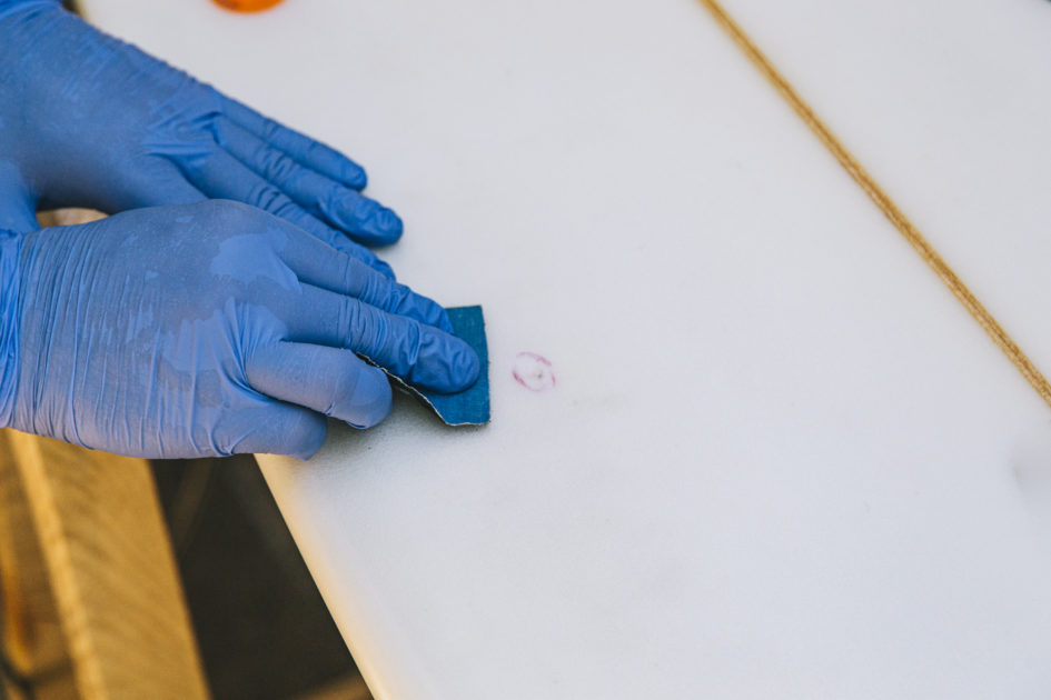 Gloved hands removing sticky residue from surface using a gentle scrub pad