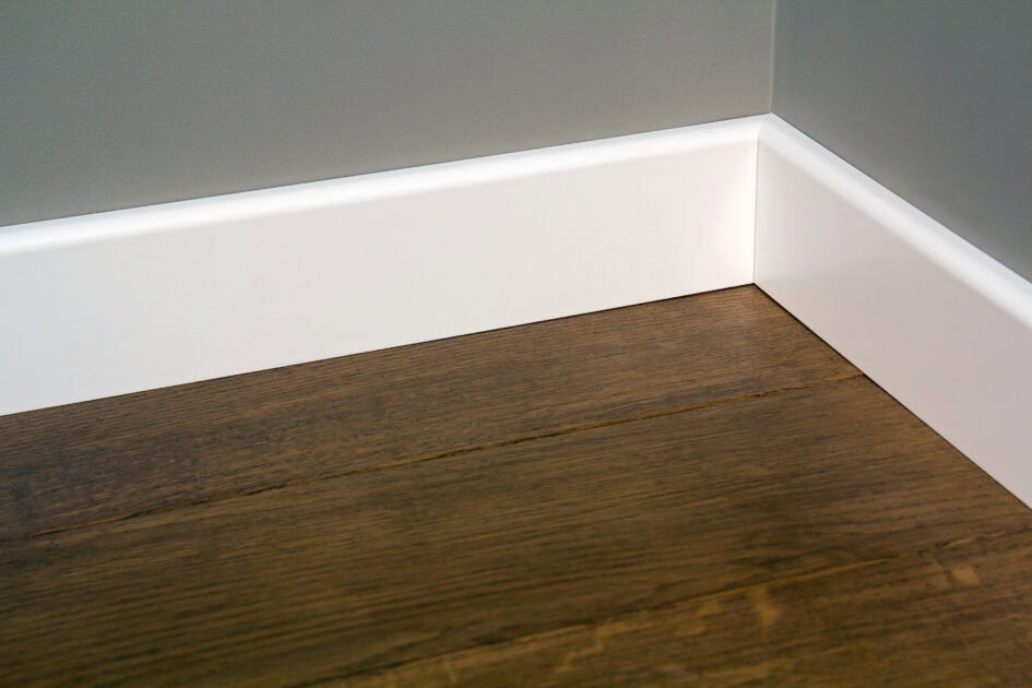 Clean white baseboards on a wood floor after thorough dusting and wiping.