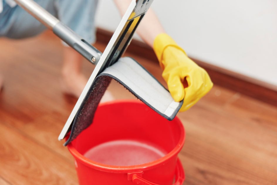 A person using a mop and wringing it into a red bucket while cleaning the floor.