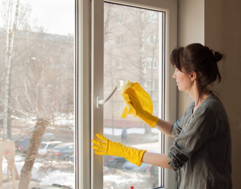 Woman cleaning interior side of window with yellow gloves during winter grime removal