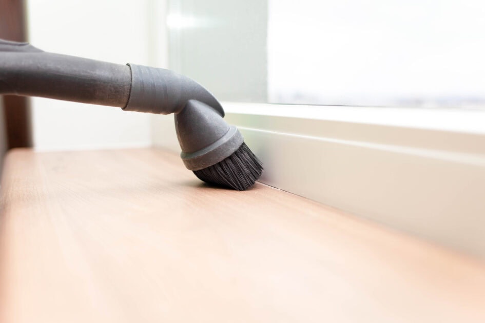 Vacuuming baseboards with a brush attachment to remove built-up dust and dirt.