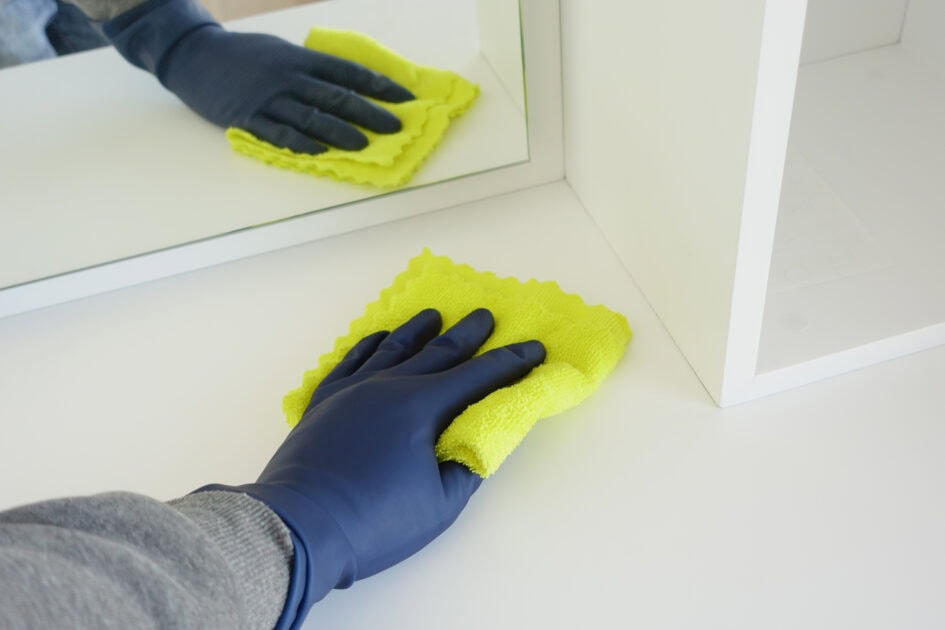 hand in blue rubber gloves cleaning corners with cloth